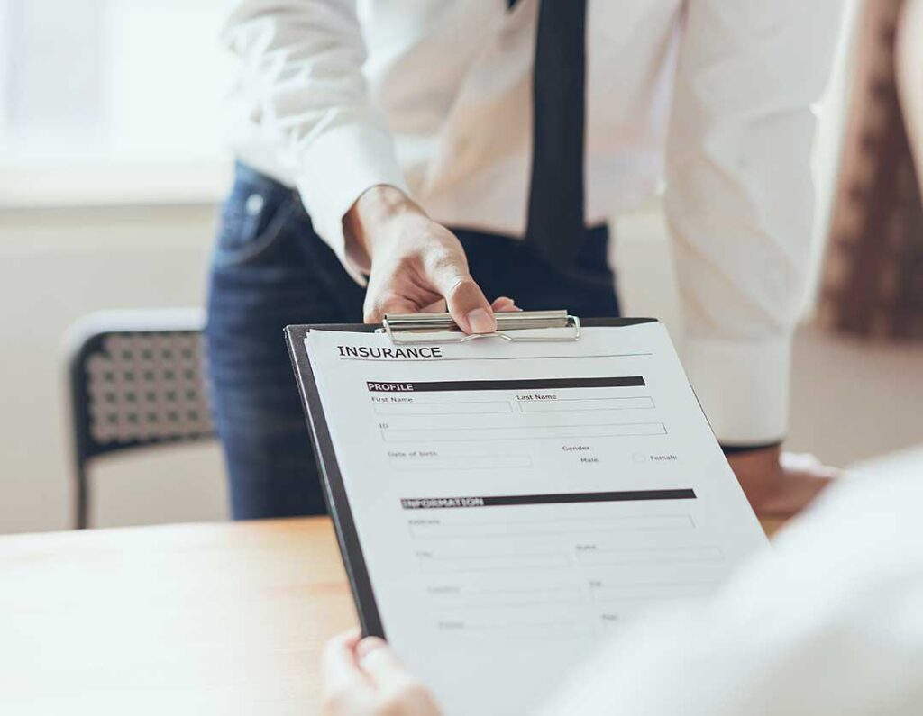 Insurance documents, a vehicle damage estimate, and a person reviewing a claim notice at a kitchen table