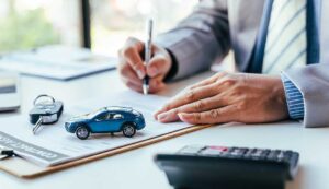 A homeowner reviews a renewal policy beside a calculator, vehicle keys, and house documents.